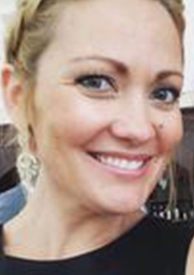 Close-up of a smiling woman with blonde hair, wearing earrings and minimal makeup.