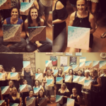 A group of women displaying their paintings at an art class, each holding up their artwork with smiles in a room with a wooden floor.